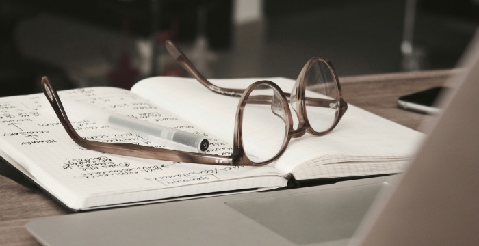 A pair of glasses and a white pen on a notebook